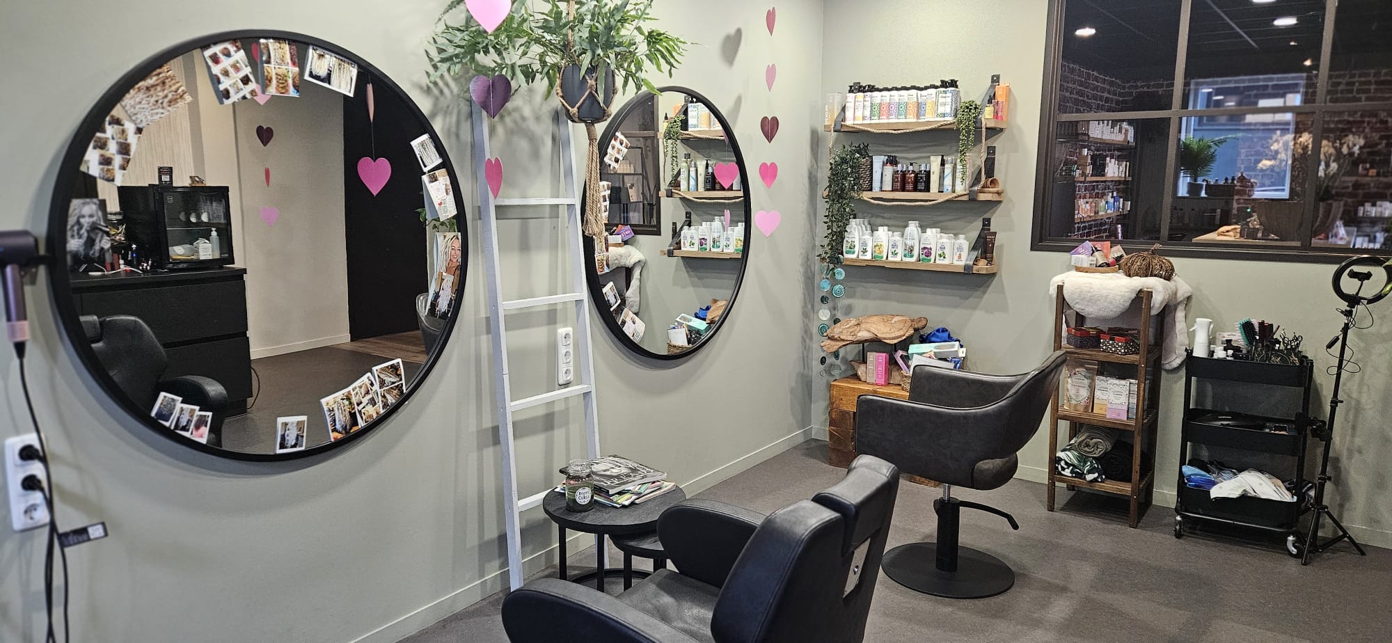 De salonruimte van Roots & Curls met ronde zwarte spiegels, planten en productschappen